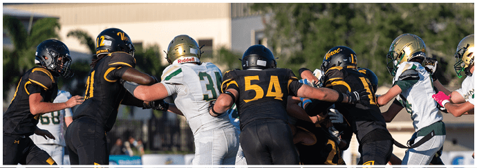 People wearing football helmets and uniforms are engaged in a play on a football field with some players pushing against each other. Descripci n generada con IA