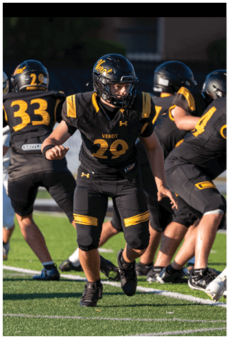 People wearing black and yellow football uniforms with helmets are actively engaged in a game on a grassy field. Descripci n generada con IA