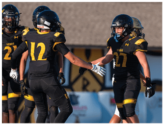 Two people in black and yellow football uniforms are reaching out to each other on a field with other players in the background. Descripci n generada con IA