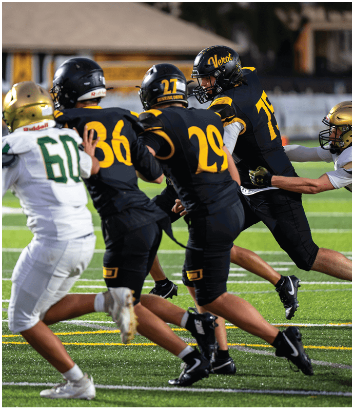 Four football players in helmets and uniforms are engaged in a play on a field, with three wearing black and yellow and one in white and green. Descripci n generada con IA