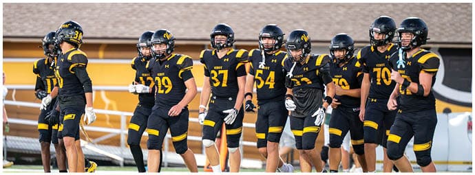 A group of people wearing black and yellow football uniforms and helmets are standing together on a field. Descripci n generada con IA