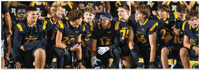 A group of people wearing matching sports uniforms sit closely together on bleachers, engaged in conversation and appearing attentive. Descripci n generada con IA