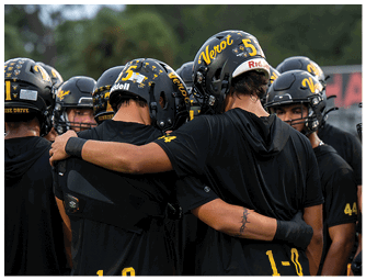 A group of people wearing black football helmets and black shirts are huddled together outdoors. Descripci n generada con IA