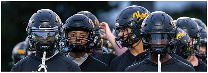 A group of people wearing black sports helmets and matching black jerseys with yellow lettering stand closely together outdoors. Descripci n generada con IA