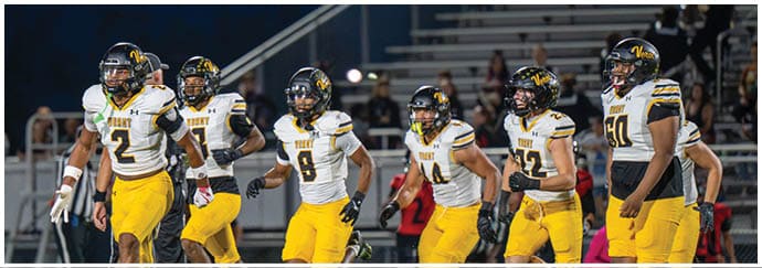 A group of football players in yellow pants and white jerseys are running together on a field during a game. Descripci n generada con IA