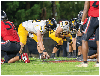 People in football uniforms are positioned on a grassy field preparing for a play during a game. Descripci n generada con IA
