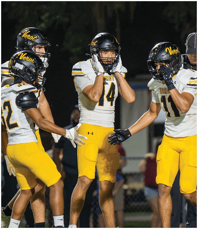 Four people in yellow and white football uniforms are standing on a field at night with one person in a referee uniform nearby. Descripci n generada con IA