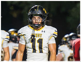 A person wearing a black football helmet and a white football jersey with the number 11 stands on a field with other players in the background. Descripci n generada con IA