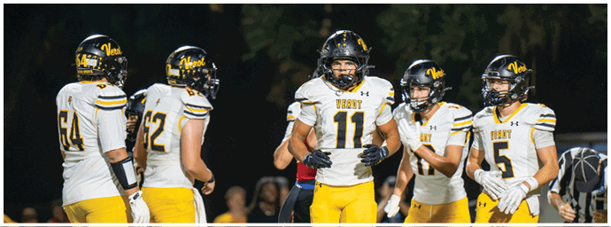 Five people wearing white and yellow football uniforms are standing together on a field at night. Descripci n generada con IA