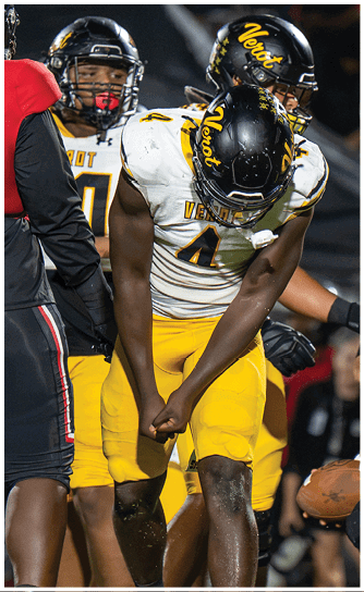 A person in a yellow and white football uniform with the number 4 on the jersey is clenching their fists and looking down on a football field during a game. Descripci n generada con IA