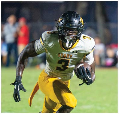 A person wearing a football uniform with the number 3 is running on a grassy field while holding a football, with a referee standing nearby. Descripci n generada con IA