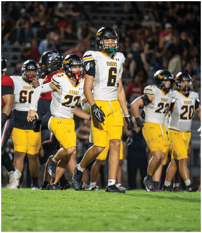 A group of adults wearing yellow football pants and white jerseys with black helmets are walking on a field during a game. Descripci n generada con IA