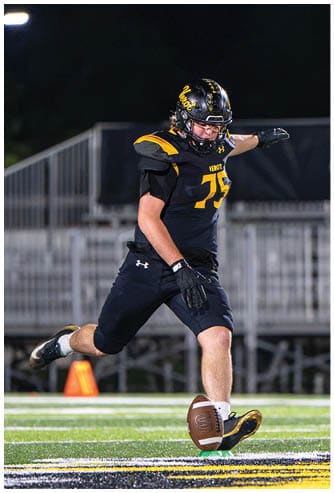 A person in a black and yellow football uniform is kicking a football on a field at night. Descripci n generada con IA