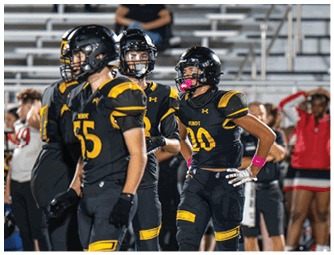 Several people in black and yellow football uniforms stand on a field with a referee and others in the background during a game. Descripci n generada con IA
