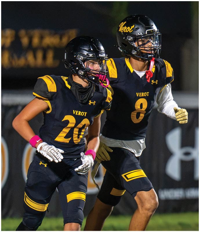 Two people wearing black and yellow football uniforms with helmets are on a field, appearing to be in motion during a game. Descripci n generada con IA