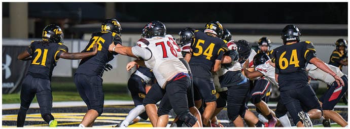 People wearing football uniforms are engaged in a play on a field under stadium lights. Descripci n generada con IA