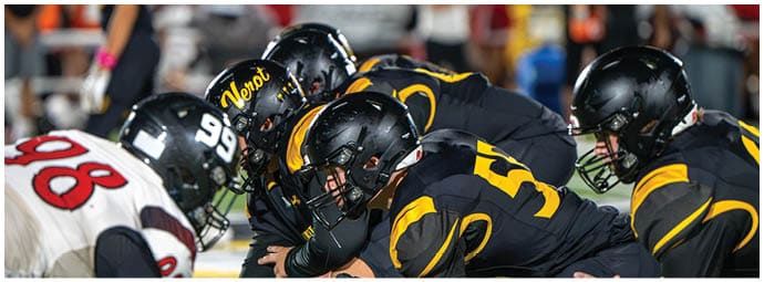 Several people in black and yellow football uniforms are lined up on the field facing opponents in white and red uniforms during a game. Descripci n generada con IA