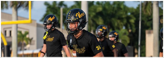 People wearing black football helmets and uniforms are standing on a field with palm trees and a goalpost in the background. Descripci n generada con IA