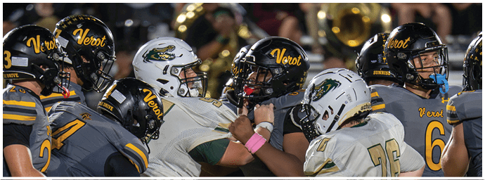 Several football players in helmets and uniforms are engaged in a close, intense moment on the field during a game. Descripci n generada con IA