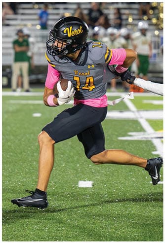 A person wearing a football uniform with the number 14 is running on a field while holding a football. Descripci n generada con IA