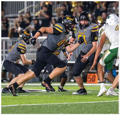 Several people in football uniforms are actively engaged in a play on a well-lit field during a game. Descripci n generada con IA