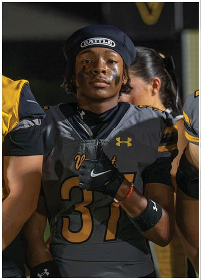 A person wearing a football uniform and a beret with the word “BATTLE" on it has black face paint under their eyes and is looking forward with a serious expression. Descripci n generada con IA