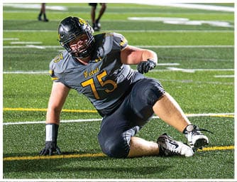 A person wearing a football uniform with the number 75 is sitting on the turf field during a game or practice. Descripci n generada con IA