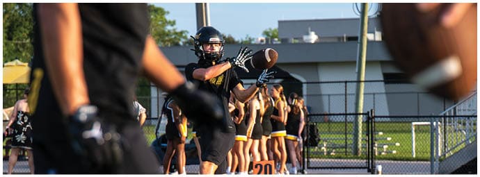 People wearing black sports uniforms are practicing football outdoors with one person preparing to throw a football. Descripci n generada con IA