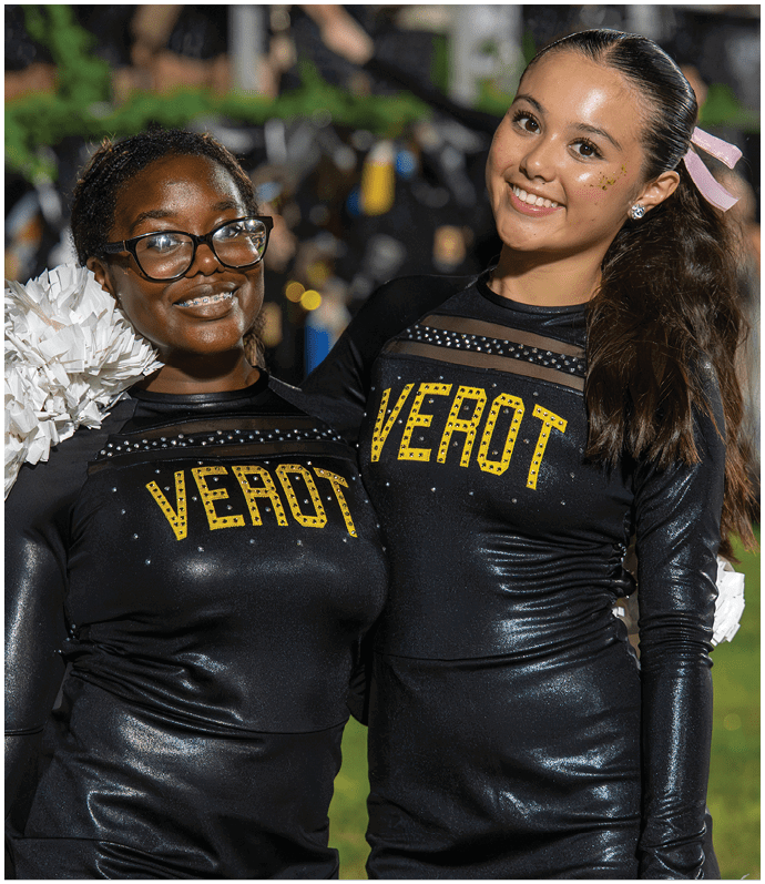 Two people wearing matching black cheerleading uniforms with yellow lettering and smiling while posing together. Descripci n generada con IA