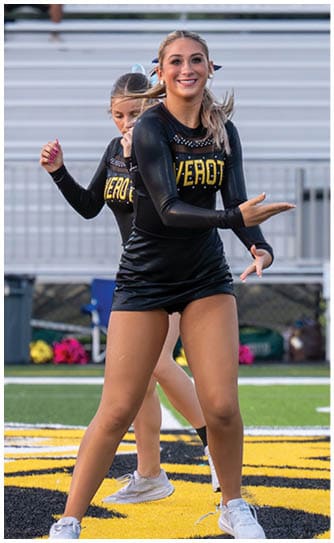 Three people in black and yellow football uniforms are on a green field with one person holding a football in a ready position while the others prepare to move. Descripci n generada con IA