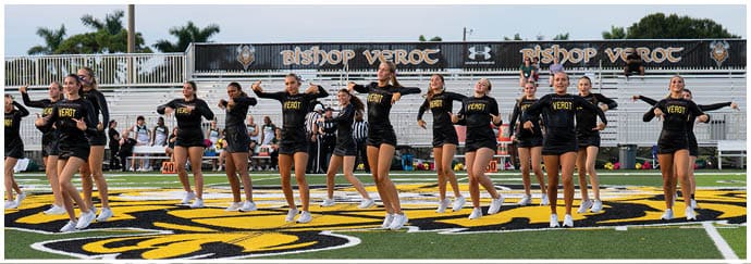 A group of people wearing black shorts and shoes are standing on a sports field with a large yellow and black logo on the turf. Descripci n generada con IA