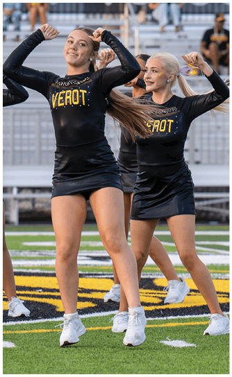 Two people in matching black cheerleading outfits with the word “VEROT" in yellow are performing a routine outdoors. Descripci n generada con IA