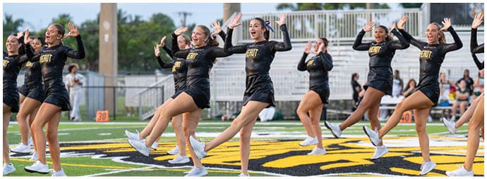 People wearing athletic shoes and shorts are performing a synchronized dance or exercise routine on a sports field with a large logo. Descripci n generada con IA