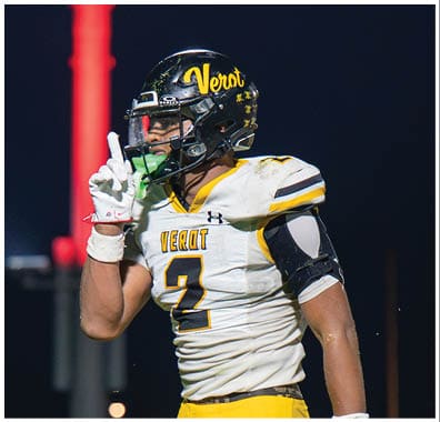 A person wearing a football uniform with a helmet and yellow pants is holding one finger up while standing on a field at night. Descripci n generada con IA