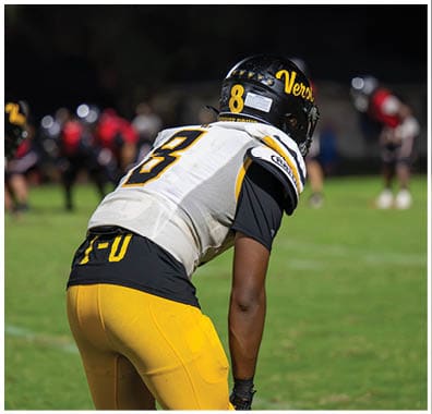Two people in football uniforms are positioned on a field, appearing ready for a play during a game at night. Descripci n generada con IA