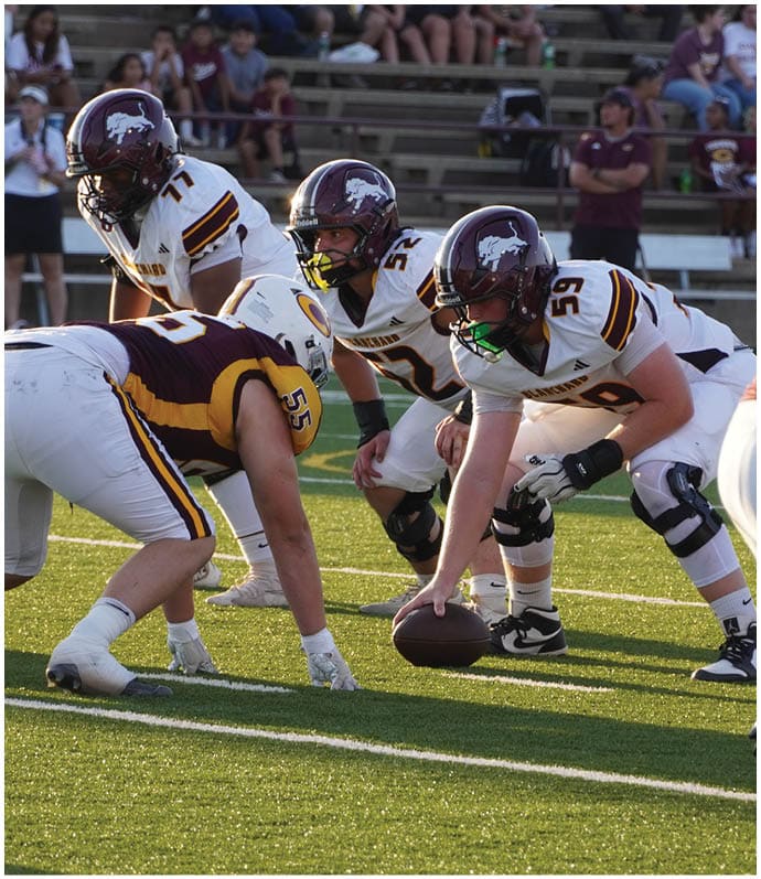 Three football players in blue and white uniforms running on a field. Description generated by AI