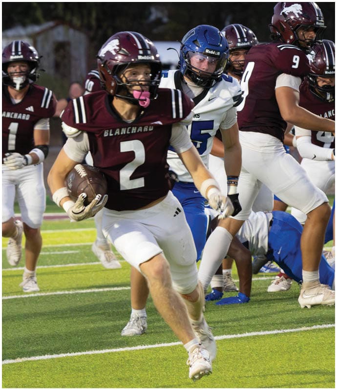 Three football players in blue and white uniforms running on a field. Description generated by AI