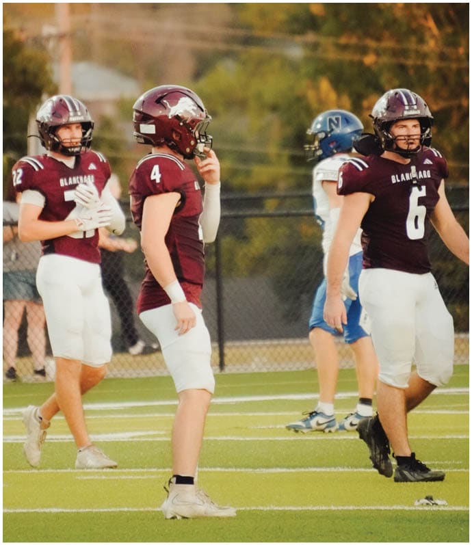 Three football players in blue and white uniforms running on a field. Description generated by AI