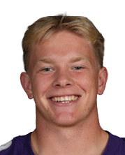 A person wearing a purple football jersey with the number 10 and the word Bloomington on the front is smiling with hands behind their back. Description generated by AI