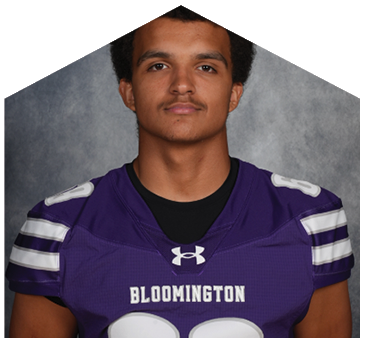 Person wearing a purple Bloomington sports jersey with white stripes on the shoulders and the Under Armour logo on the chest. Description generated by AI