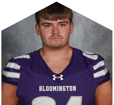 Person wearing a purple Bloomington football jersey with the number 64 stands against a gray backdrop. Description generated by AI