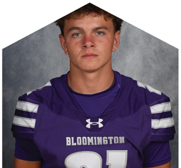 Person wearing a purple sports jersey with the word Bloomington and the number 21 on it, standing against a gray background. Description generated by AI
