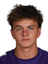 Person with short curly hair wearing a purple Bloomington football jersey with the number 21 standing against a white background. Description generated by AI