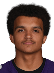 A person with short curly hair wearing a purple football jersey with the number 69 and the word Bloomington on the front stands facing forward against a white background. Description generated by AI