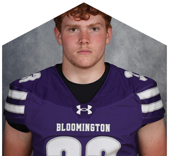 A person with curly hair wearing a purple Bloomington football jersey with the number 33 stands against a gray background. Description generated by AI