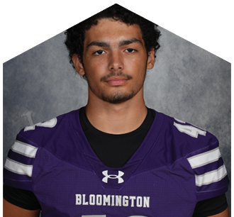 A person with curly hair wearing a purple Bloomington sports jersey with the number 42 stands against a gray textured background. Description generated by AI