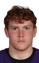 A person with curly hair wearing a purple Bloomington football jersey with the number 33 stands with hands behind their back against a white background. Description generated by AI