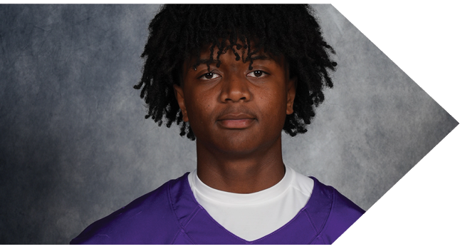Person with curly hair wearing a purple sports jersey over a white shirt against a gray textured background. Description generated by AI