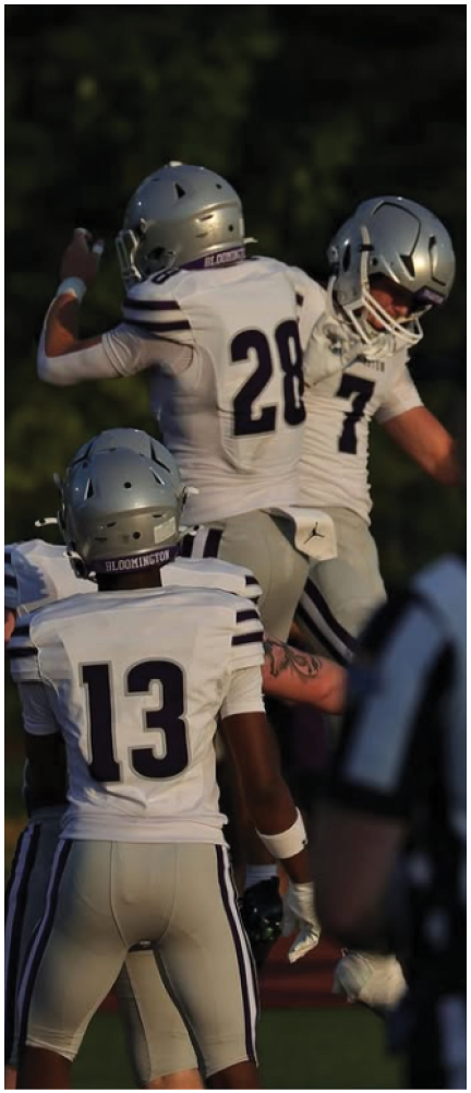 A person in a white football uniform is running on a field while a group of people stand behind a fence watching. Description generated by AI