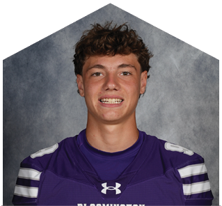 A person wearing a purple Bloomington sports jersey with white stripes on the sleeves is smiling against a gray backdrop. Description generated by AI